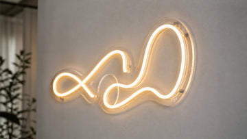 A warm white LED neon sign is mounted on a clear contour-cut acrylic backboard on a light grey wall.